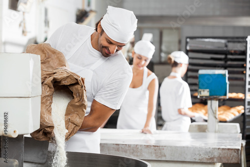 Fotografie, Obraz Male Baker Pouring Flour In Kneading Machine