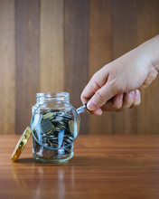 Image Of Hands With Magnifying Glass Looking For Coins In Clear Bottle Against Blurred Wooden Background. Saving Concept.
