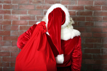 Santa Claus with bag, filled gift boxes on brick wall background