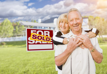 Senior Couple in Front of Sold Real Estate Sign and House