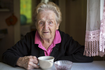 Wall Mural - Old woman drinking tea sitting in the kitchen.