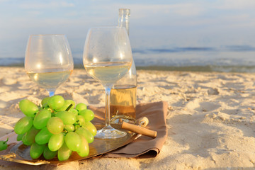 Romantic composition of white wine and grape on sandy beach