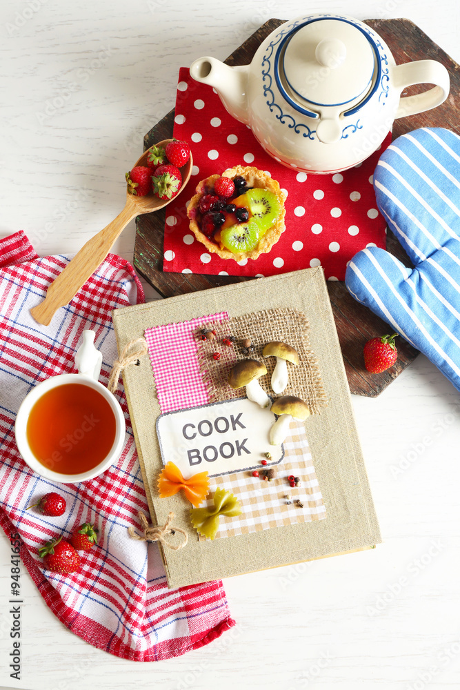 Decorated cookbook with teapot and tasty cake on the table