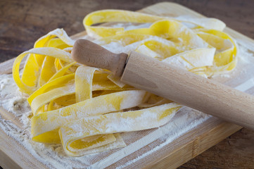 Pappardelle fatte in casa con farina, uova, e mattarello su tagliere in legno su tavolo  in legno antico