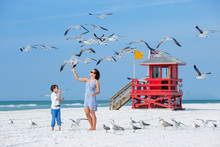 Young Mother And Her Son Feeding Seagulls On Tropical Beach