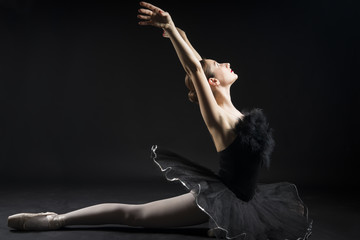 Beautiful ballerina in the role of a black swan, wearing black tutu and pointe shoes on black background