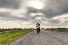 Front View Of A Motorcycle In Motion On An Asphalt Road Against The Sunset Sky