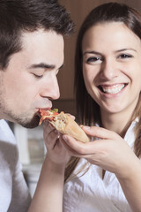 Wall Mural - Happy young couple eating pizza at the kitchen