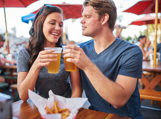 couple with beers making a toast at outdoor restaurant or pub