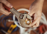 Fototapeta  - Close-up of plumber hands screwing nut of pipe with wrench over plumbing tools background. Concept of repair and technical assistance.  