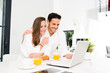 © W PRODUCTION - young couple in bathrobe at home having coffee in the kitchen and working on laptop computer