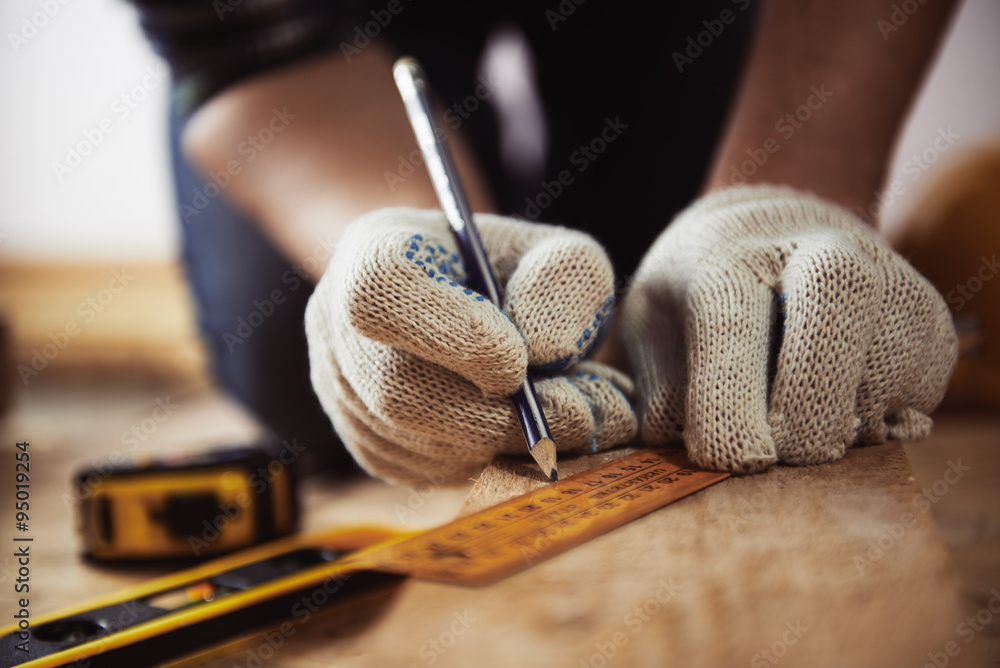 Close-up of craftsman hands in protective gloves measuring wooden plank with ruler and pencil. Woodwork and renovation concept.  - obrazy, fototapety, plakaty 