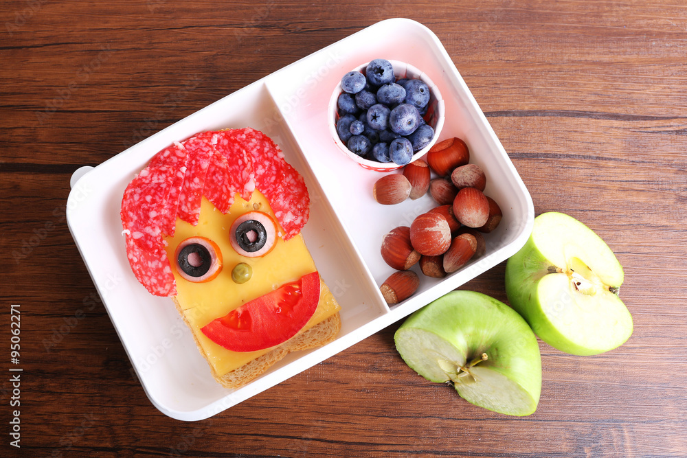 Lunchbox with creative sandwich and fruits on wooden background