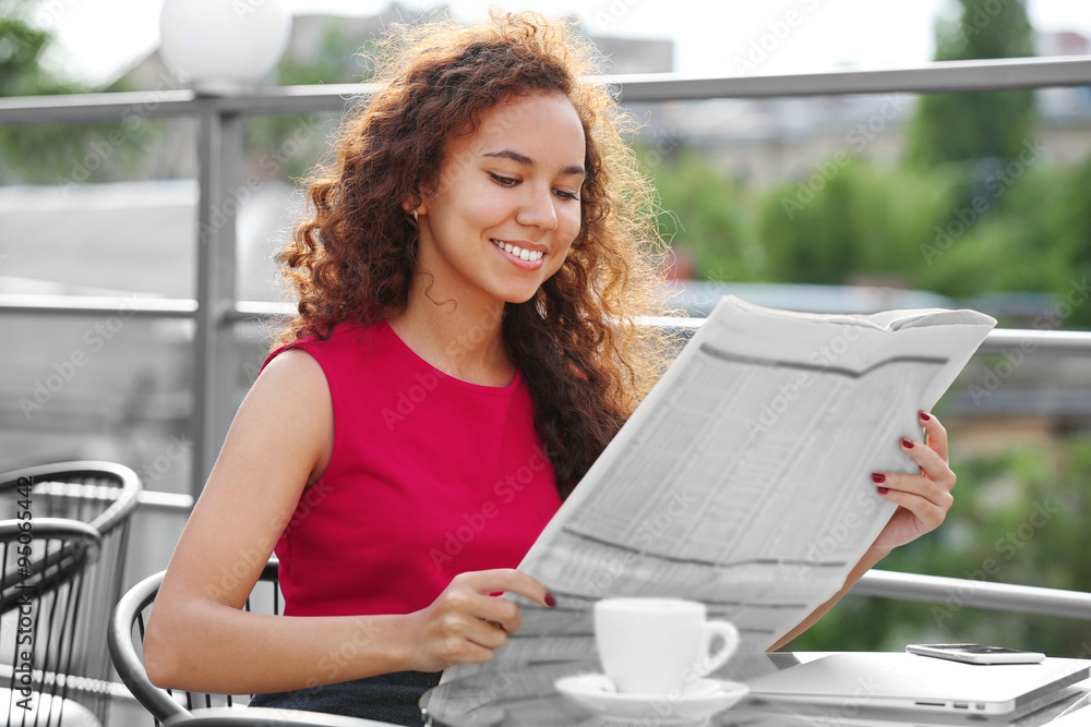 Portrait of young pretty woman in red dress reading newspaper at summer terrace