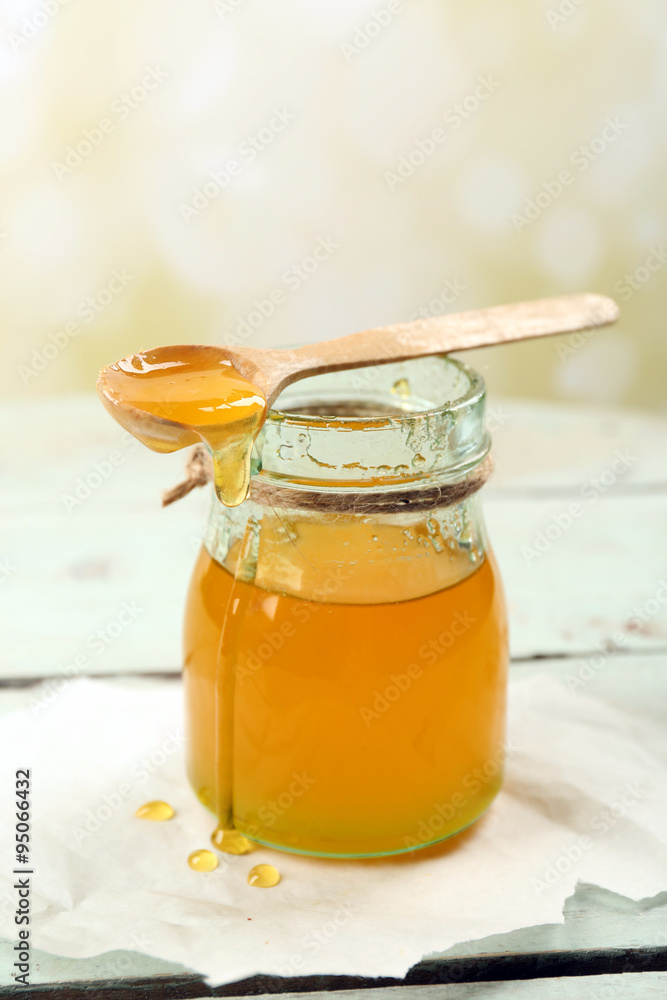 Honey jar with wooden spoon on light background