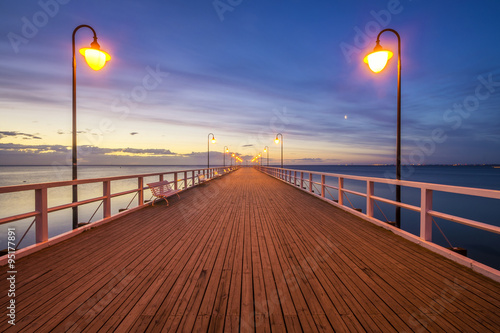 Fototapeta na wymiar wooden pier by the sea lit by stylish lamps at night 