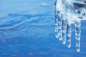 Wall Mural - Background with transparent ice icicles over water