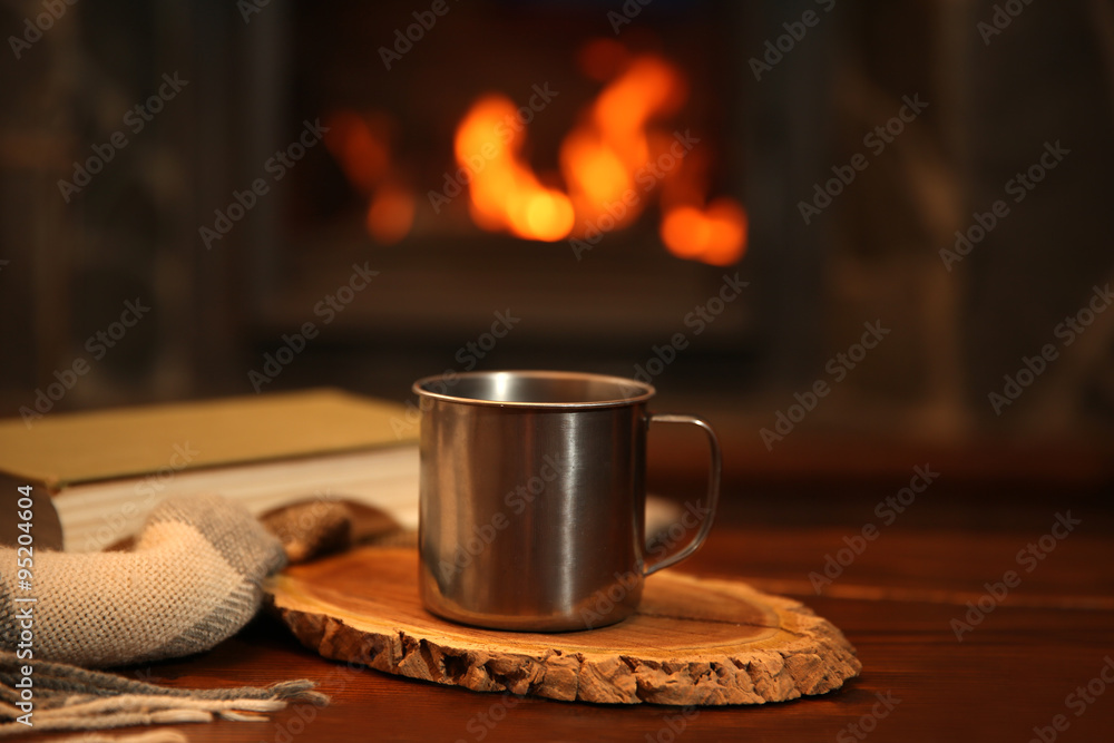 Book and mug with hot drink on vintage wood table. Fireplace as background