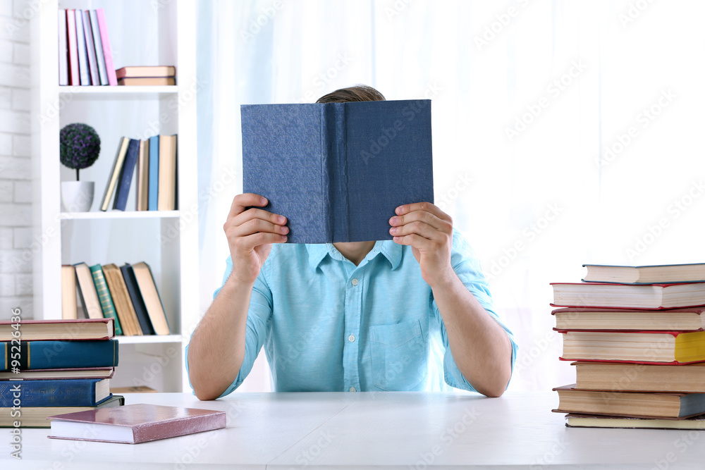 Young man reading book at table in room