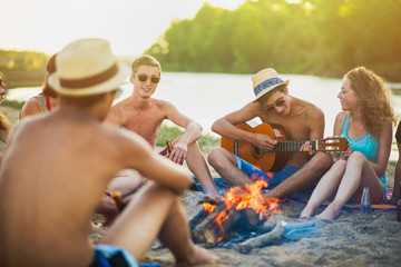 Teenagers at the beach, sings with guitare around wood fire