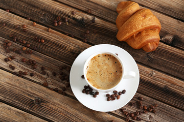 Wall Mural - Delicious croissant with cup of coffee on brown wooden backgroun