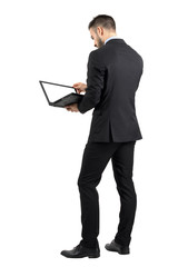 Rear view of businessman working on a laptop with blank empty screen. Full body length portrait isolated over white studio background. 