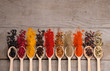 Collection of spices on spoons, on wooden background
