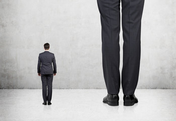 Rear view of two professionals in formal suites who stand in front of concrete wall.