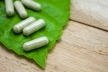 herbal medicine capsules with green herb leaf on wood table