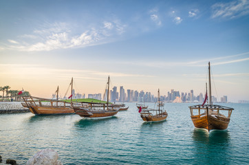 Dhows moored off Museum Park in central Doha, Qatar, Arabia, with some of the buildings from the city's commercial port in the background.