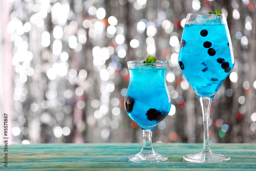 Glasses of cocktails with ice on blurred lights background