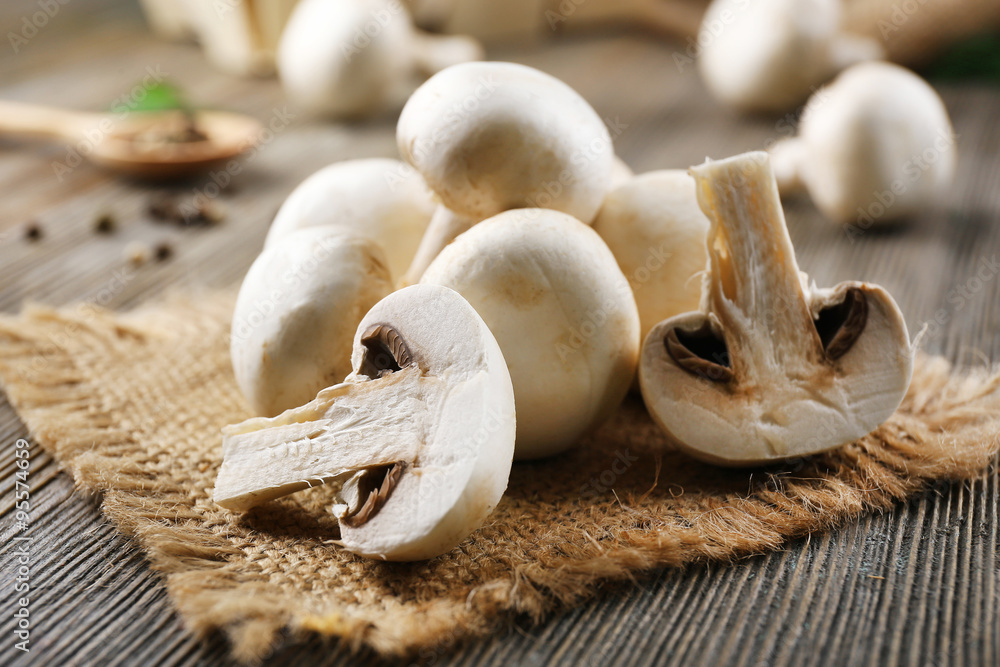 Champignon mushrooms, sacking mat and spices on wooden background