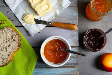 Poster - Tasty jam in the jar and bowl, butter, ripe peaches and fresh bread on wooden background close-up