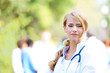 © Africa Studio - Beautiful smart woman doctor with clipboard in hands standing against blurred group of medics