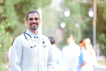 Canvas Print - Happy doctor against unfocused medical team, outdoors