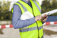 Building Surveyor In Hi Vis With Site Plans Checking His Smart Phone