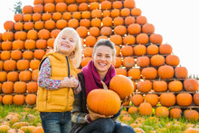 Smiling Woman And Girl Holding Pumpkins In Autumn Outdoors