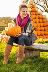 Wall Mural - Portrait of woman sitting on the bench with pumpkin on farm