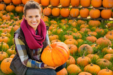 Wall Mural - Portrait of smiling woman sitting and holding big pumpkin