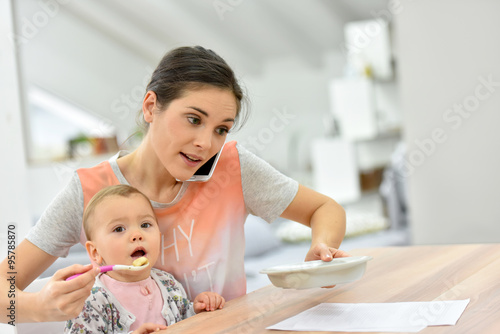 Fotografía Busy mother on the phone feeding baby a the same time