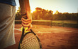 Man holding tennis racket/Close up of man holding tennis racket on clay court. In his hand is tennis ball. On court is sunset.