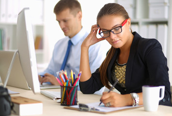 Portrait of an attractive young employee sitting in front of a computer and drawing with a colleague in the background