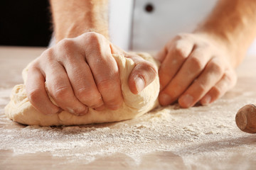 Hands kneading dough for pizza on the wooden table, close-up