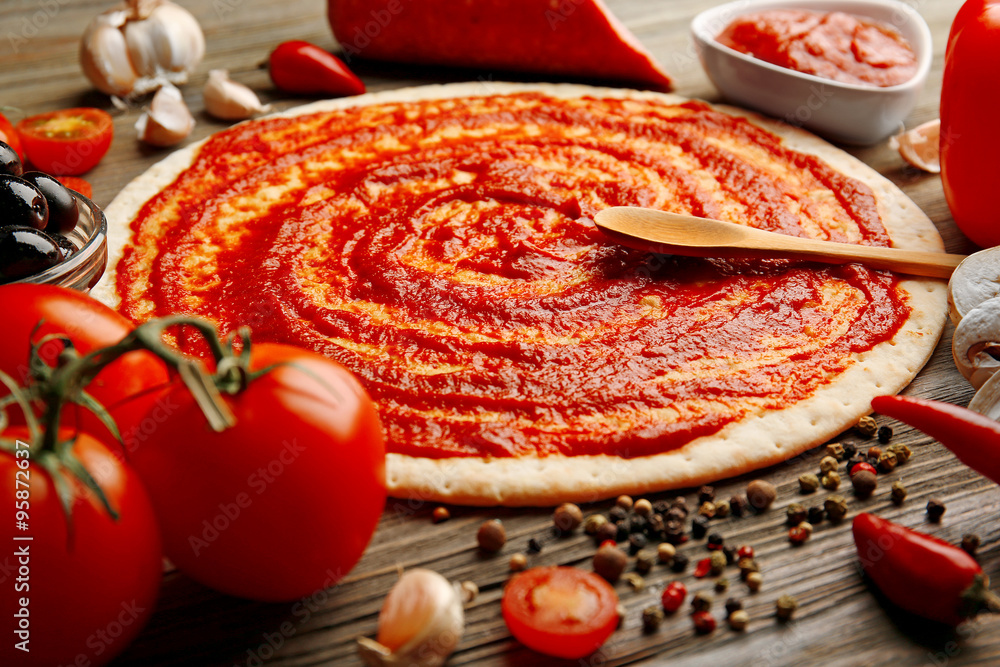 Dough basis with ketchup and ingredients for pizza, on the table