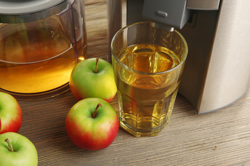 Poster - Stainless juice extractor with apples and glass of juice on wooden background, close up