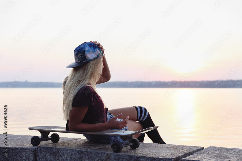Young woman with skating board on the riverside