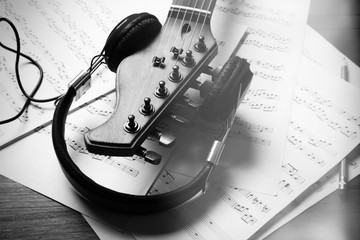 Canvas Print - Neck of acoustic guitar with headphones and music notes on table, close-up