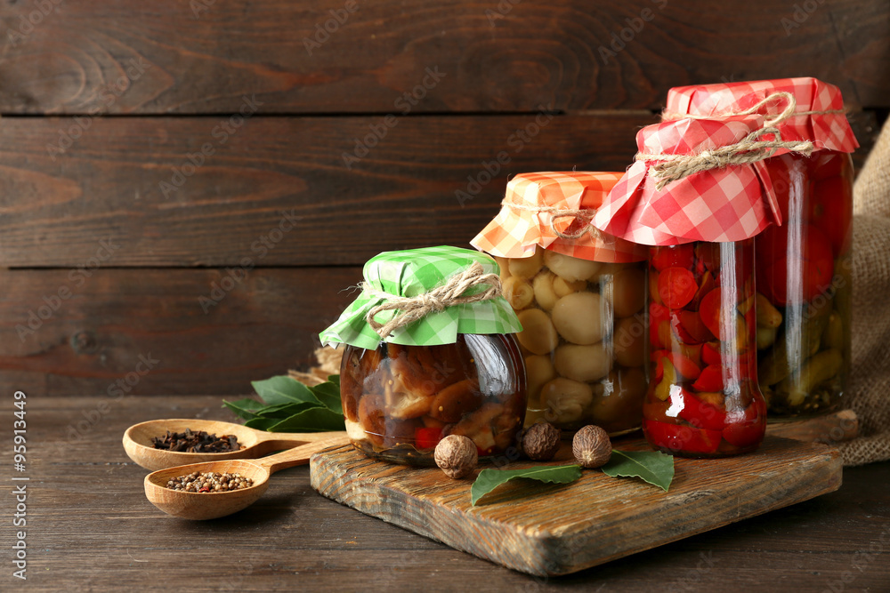 Jars with pickled vegetables and mushrooms on wooden background