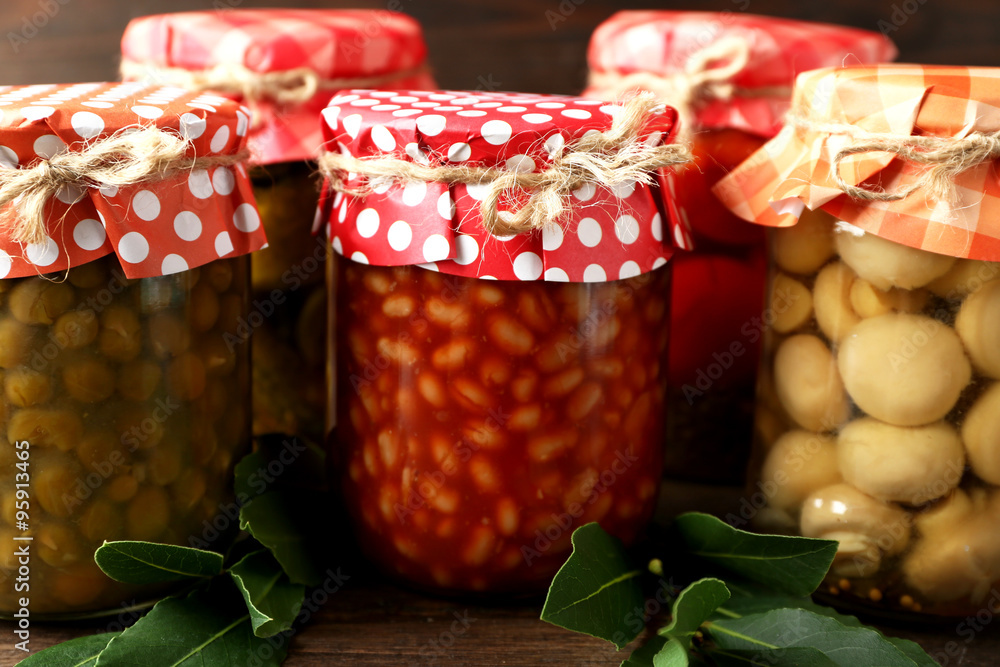 Jars with pickled vegetables and beans on wooden background