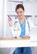 © lenets_tan - Beautiful young smiling female doctor sitting at the desk and writing